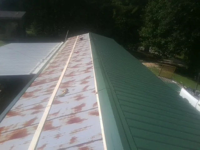 Old rusted panels beside newly installed green metal roofing — Wind Damage Roof Repair by Roofing Brothers in Baker