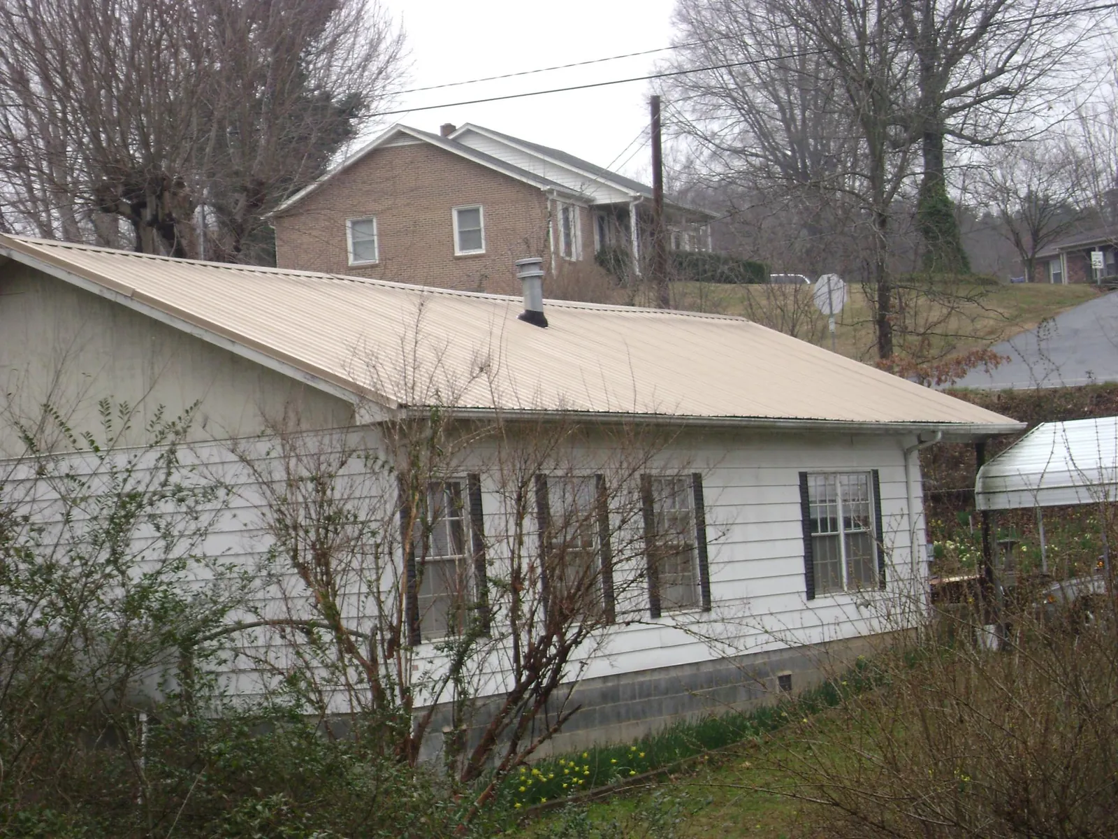 Tan metal roof on a white sided house set into a hillside — Commercial Roofing by Roofing Brothers in Baker